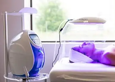 Client receiving LED light therapy beside a facial machine